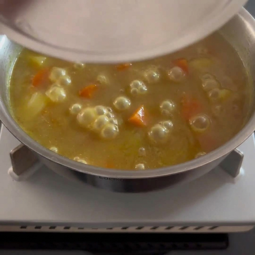 Una salsa de curry espesa y dorada siendo revuelta con trozos de papa y zanahoria visibles.