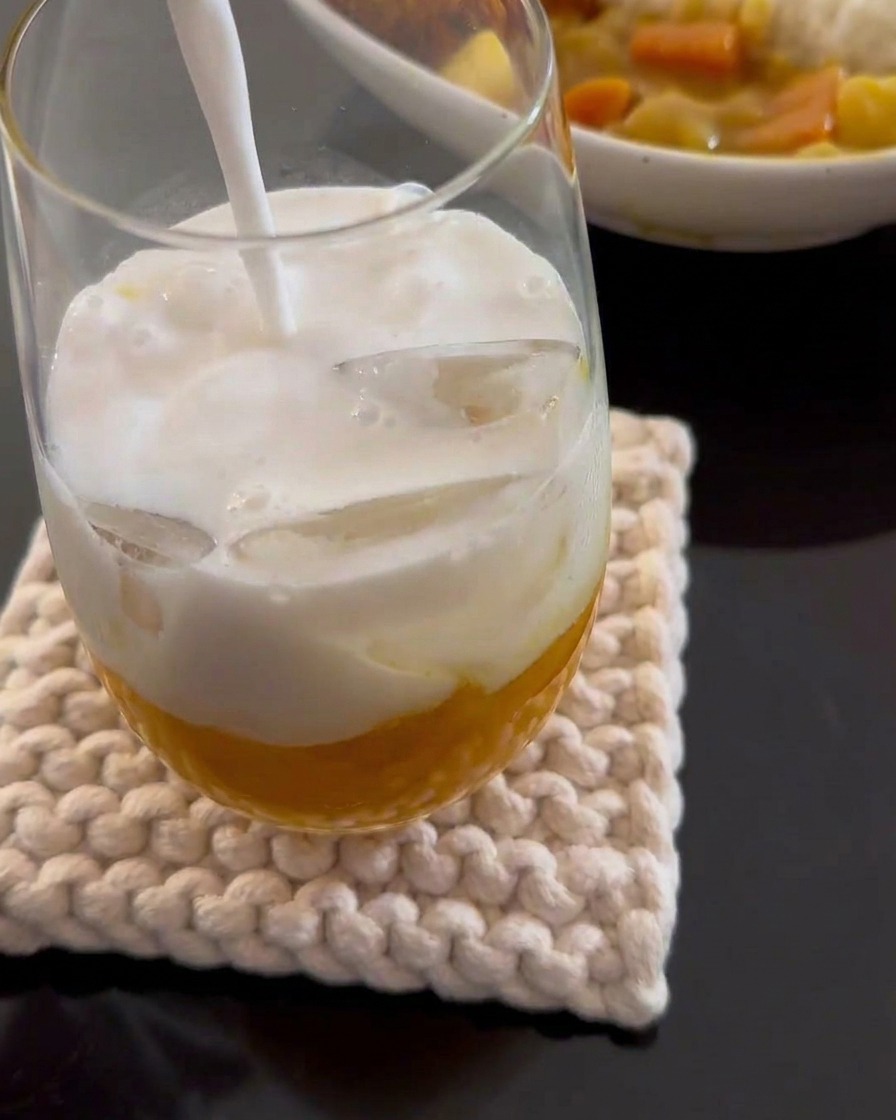 Leche de coco blanca siendo vertida en un vaso alto que contiene puré de mango amarillo y cubitos de hielo.