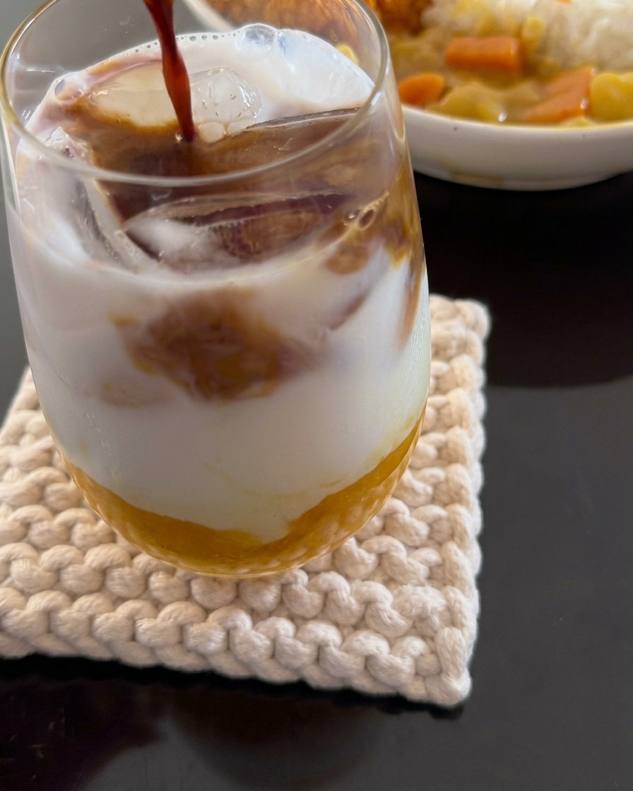 Un primer plano mostrando espresso siendo vertido en una bebida en capas que consiste en pulpa de mango, leche de coco y hielo.