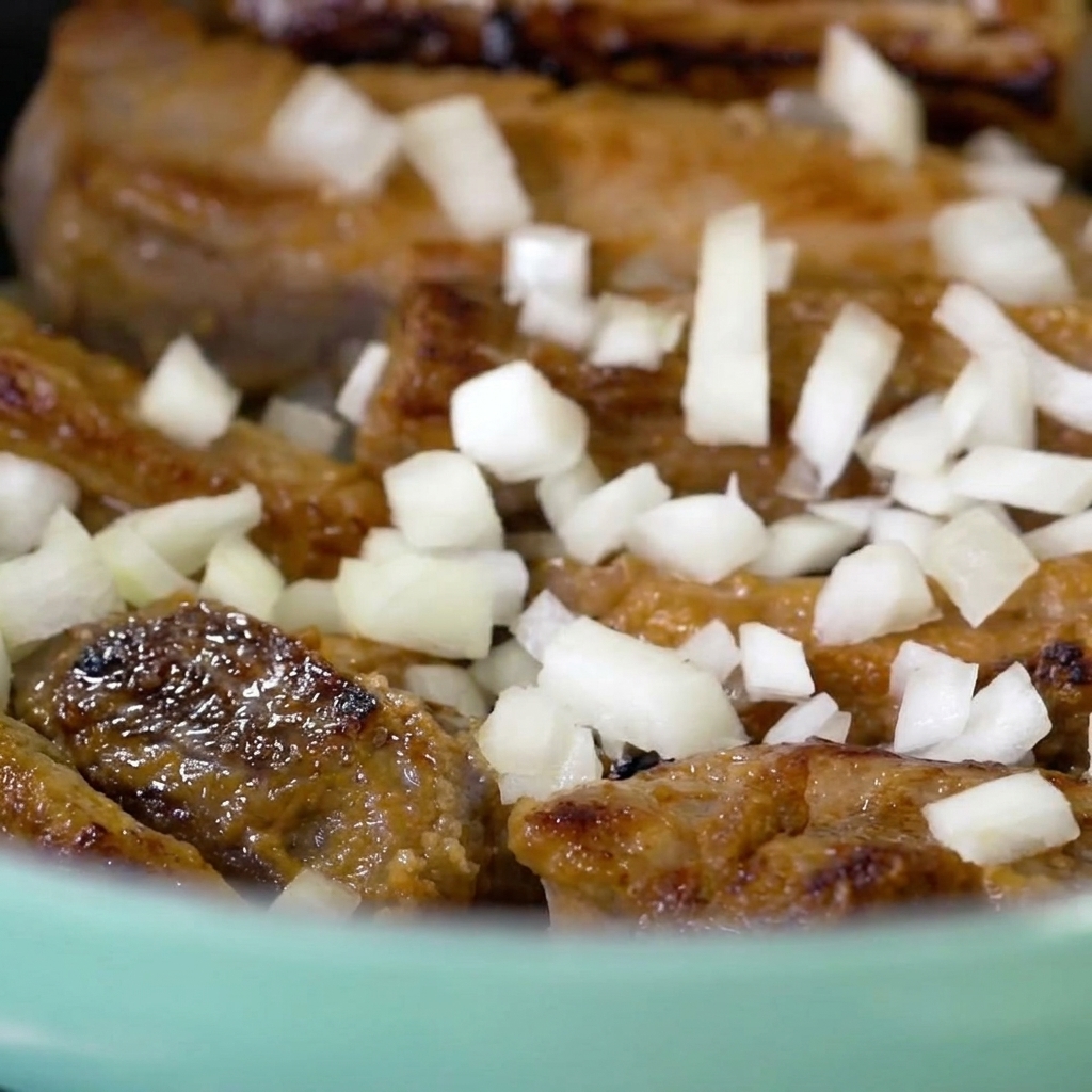 Cebolla picada siendo esparcida sobre las costillas selladas.