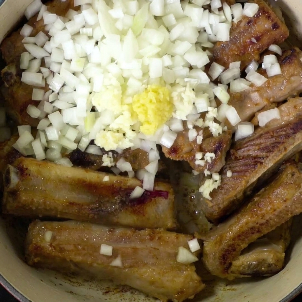 Vista cenital de las costillas en la olla con cebollas, jengibre y ajo.