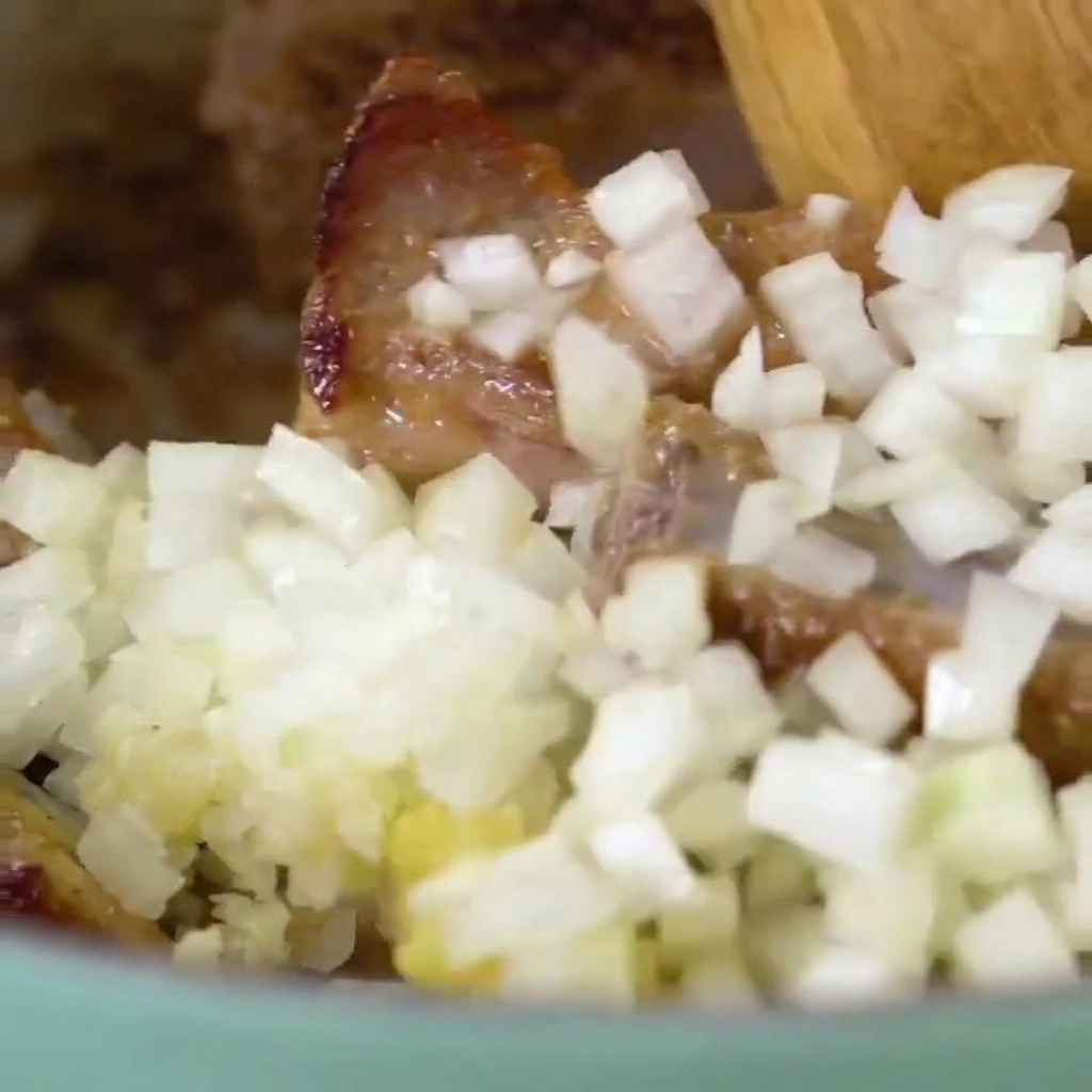 Cuchara de madera mezclando las costillas con la cebolla y el ajo.