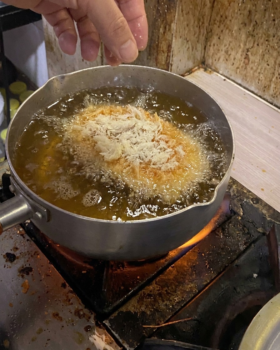 Una chuleta de cerdo empanizada se introduce suavemente en una olla con aceite caliente burbujeante.