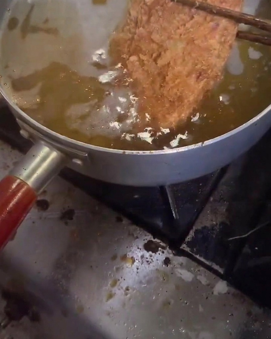 Una chuleta de cerdo friéndose por segunda vez en aceite muy caliente y burbujeante.