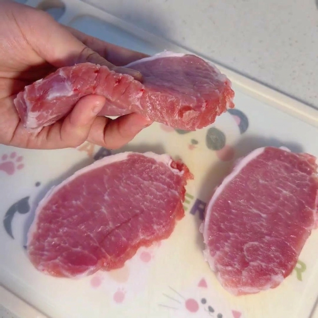 Rodajas gruesas de lomo de cerdo crudo sobre una tabla de cortar.