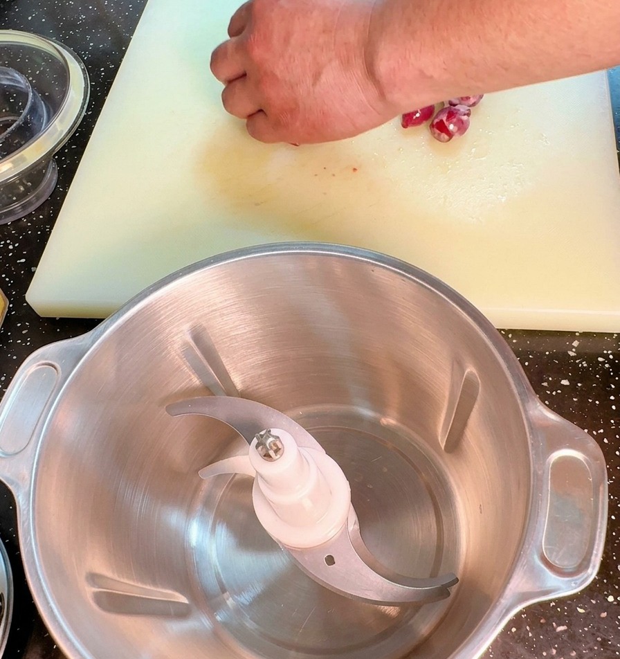 Primer plano de una mano picando finamente una cebolla roja con un cuchillo de cocina sobre una tabla blanca.