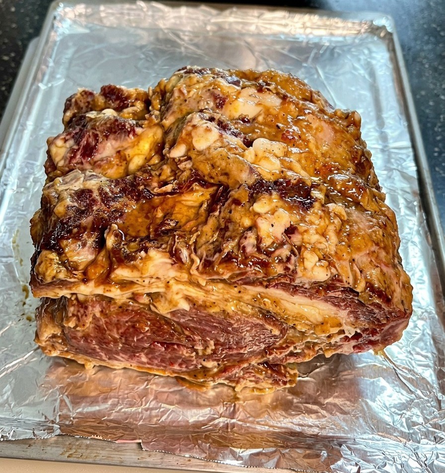 Pieza de ternera marinada con salsa y cebolla sobre una bandeja de horno forrada con papel de aluminio arrugado.