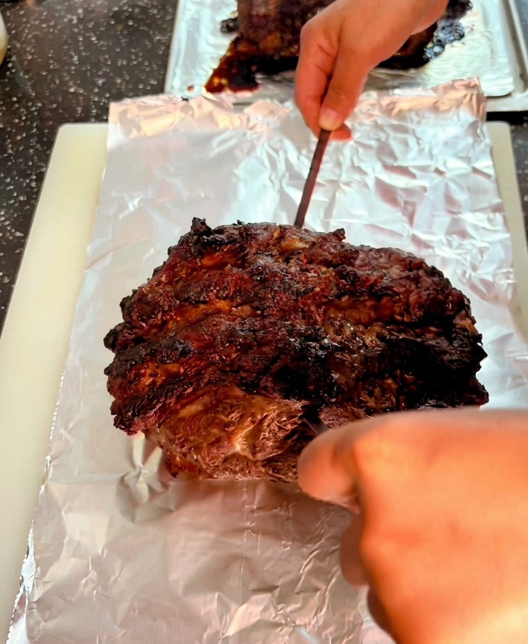 Una brocheta metálica atravesando la superficie oscura y chamuscada de un gran asado de ternera sobre papel de aluminio.