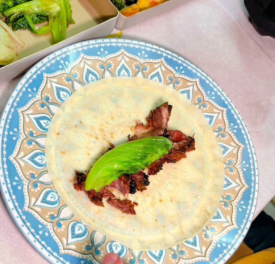 Vista superior de un plato con una tortilla rellena de jugosas lonchas de ternera ahumada y una hoja verde fresca.