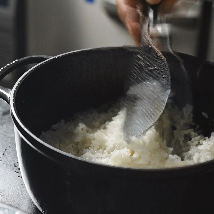 Una mano usando una pala de arroz para remover arroz caliente en una olla.