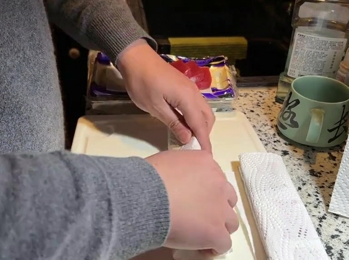 Manos presionando papel de cocina contra un bloque de atún crudo sobre una tabla.