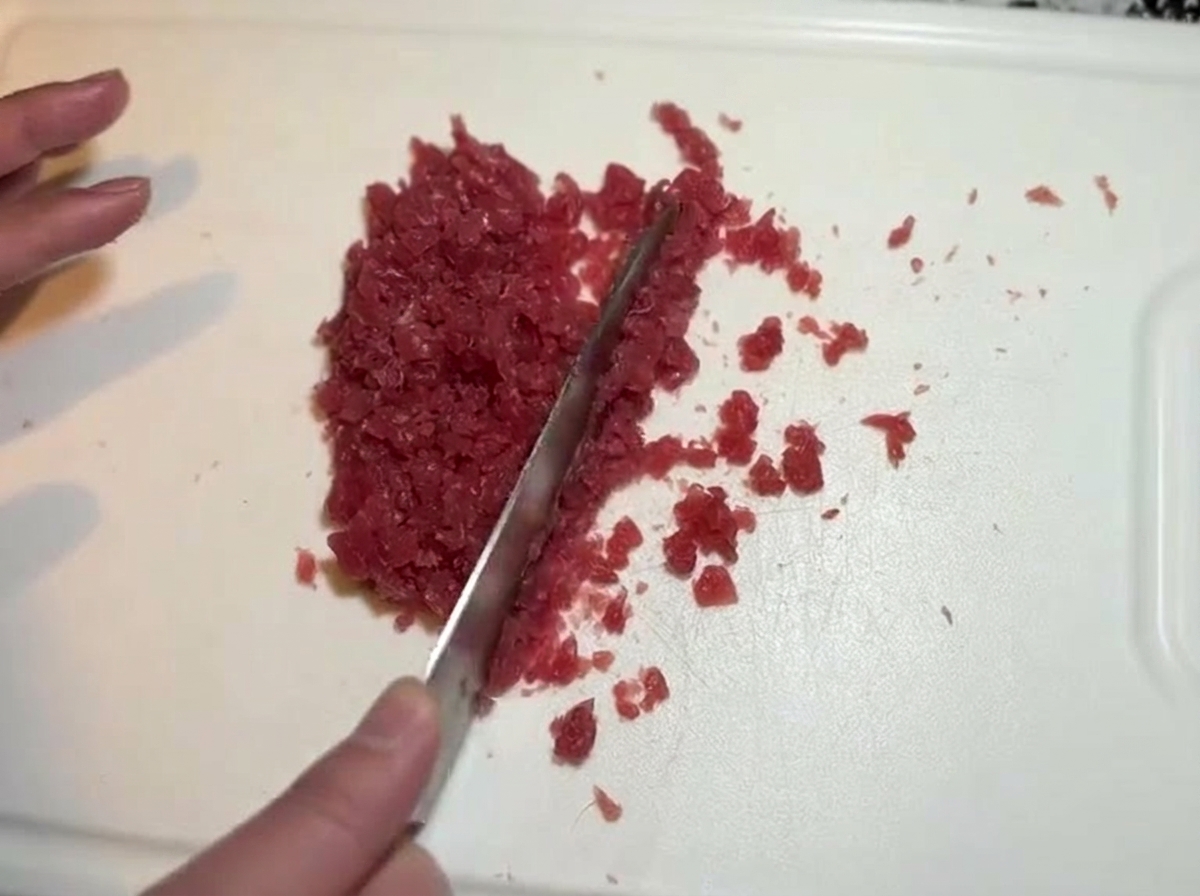 Un cuchillo picando finamente el atún hasta obtener una textura de pasta.