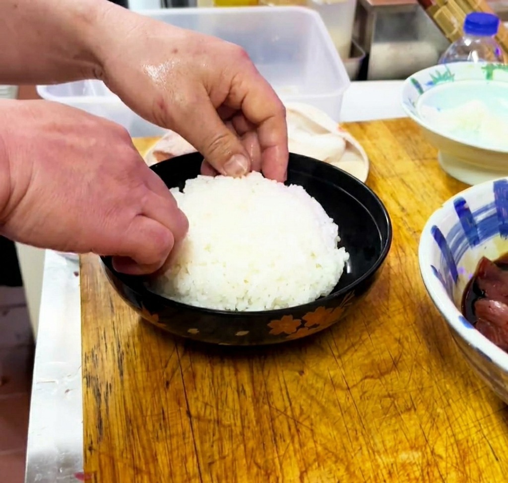 Arroz blanco cocido siendo nivelado suavemente dentro de un bol negro de servir.