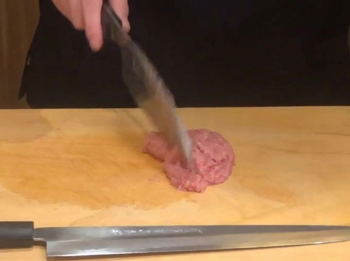 Mano de un chef usando un cuchillo afilado para picar atún crudo sobre una tabla de madera.