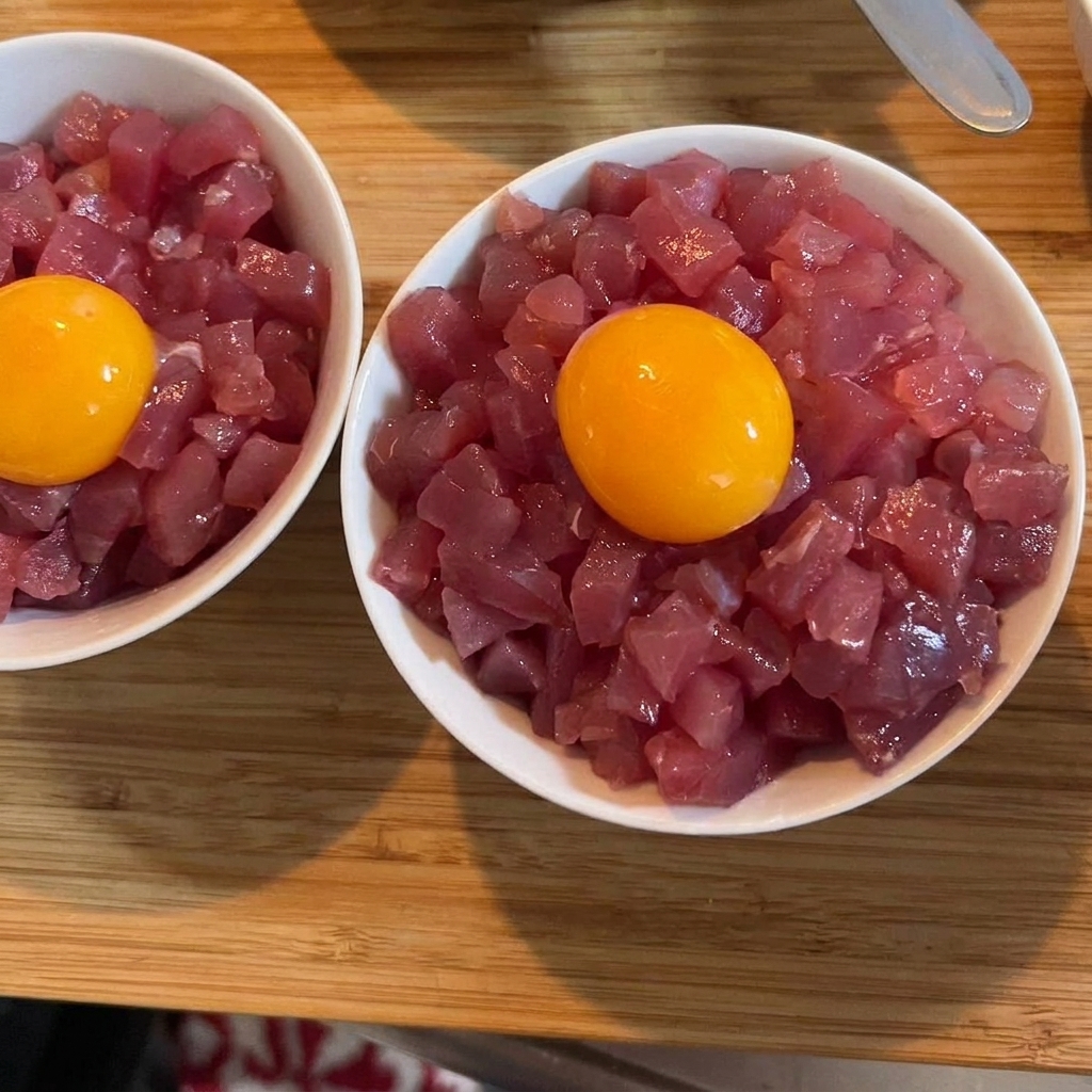 Una vibrante yema de huevo cruda y dorada posada sobre un bol de atún y arroz, adornada con cebolleta verde.