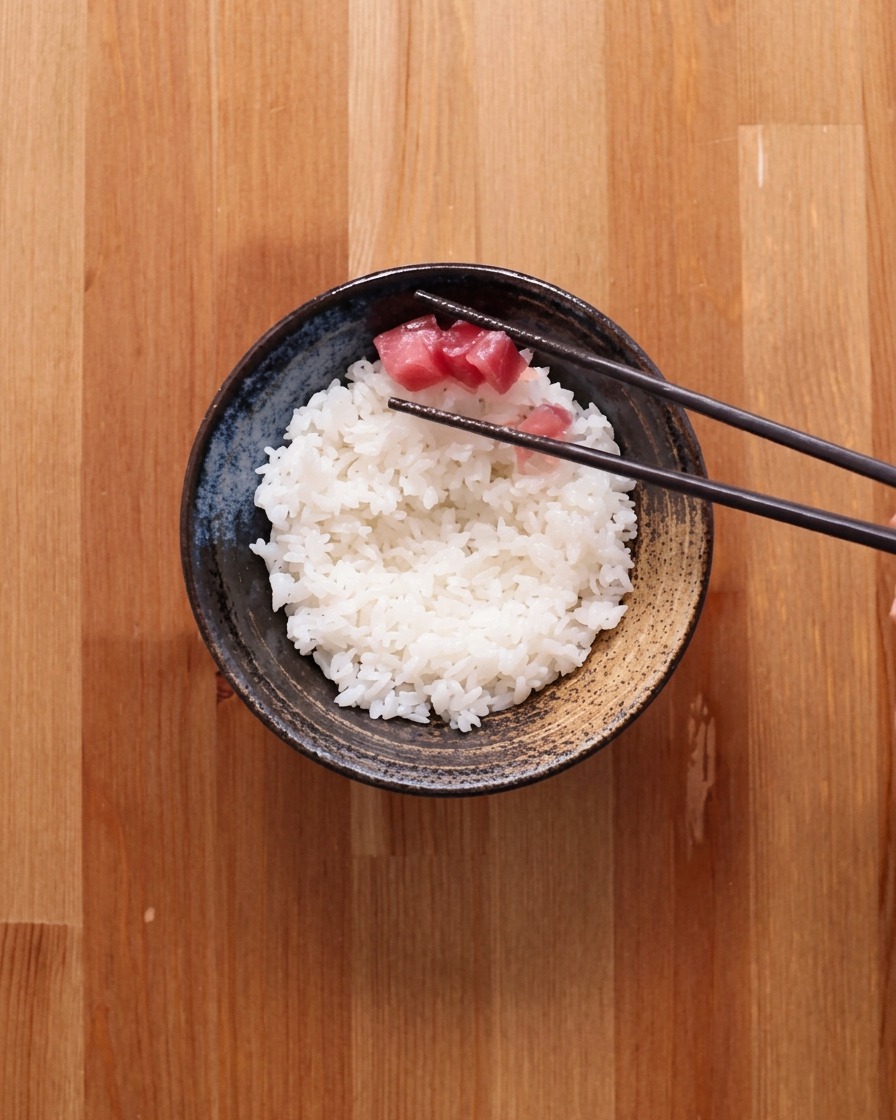 Un tazón de arroz blanco parcialmente cubierto con una capa de atún crudo en cubos.