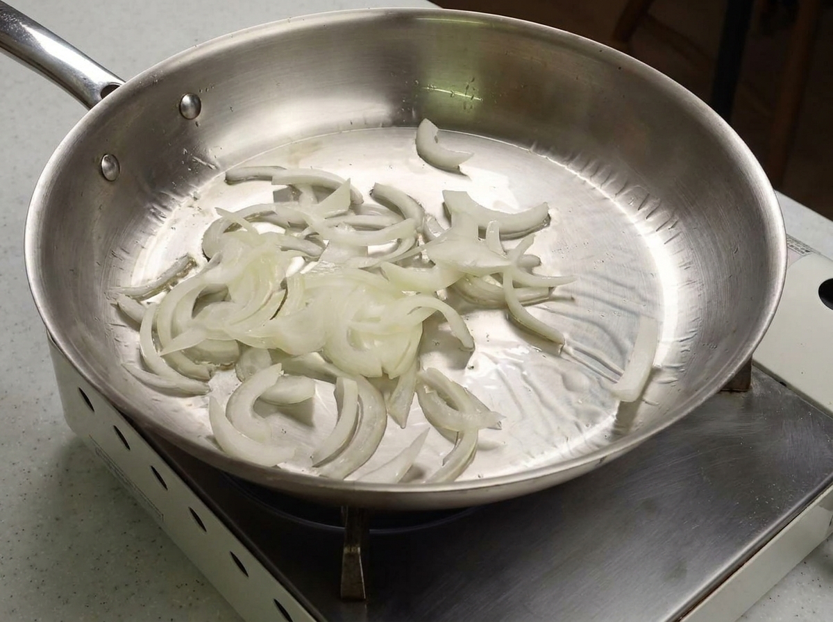 Tiras de cebolla siendo salteadas en una sartén.
