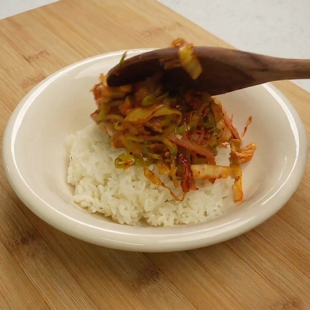 Cuchara sirviendo el salteado sobre un bol de arroz.