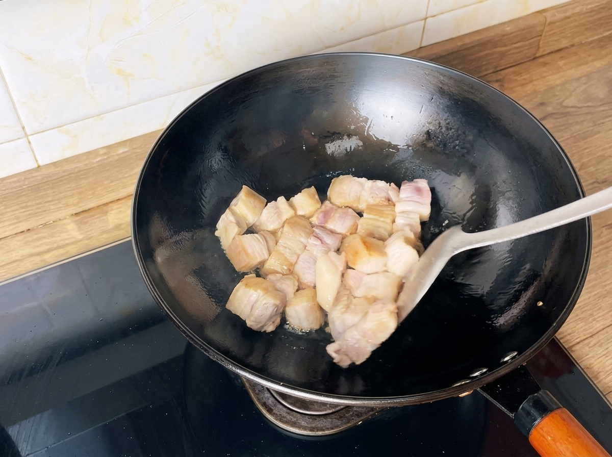 Cubos de panceta de cerdo salteándose en un wok con una espátula hasta dorarse.