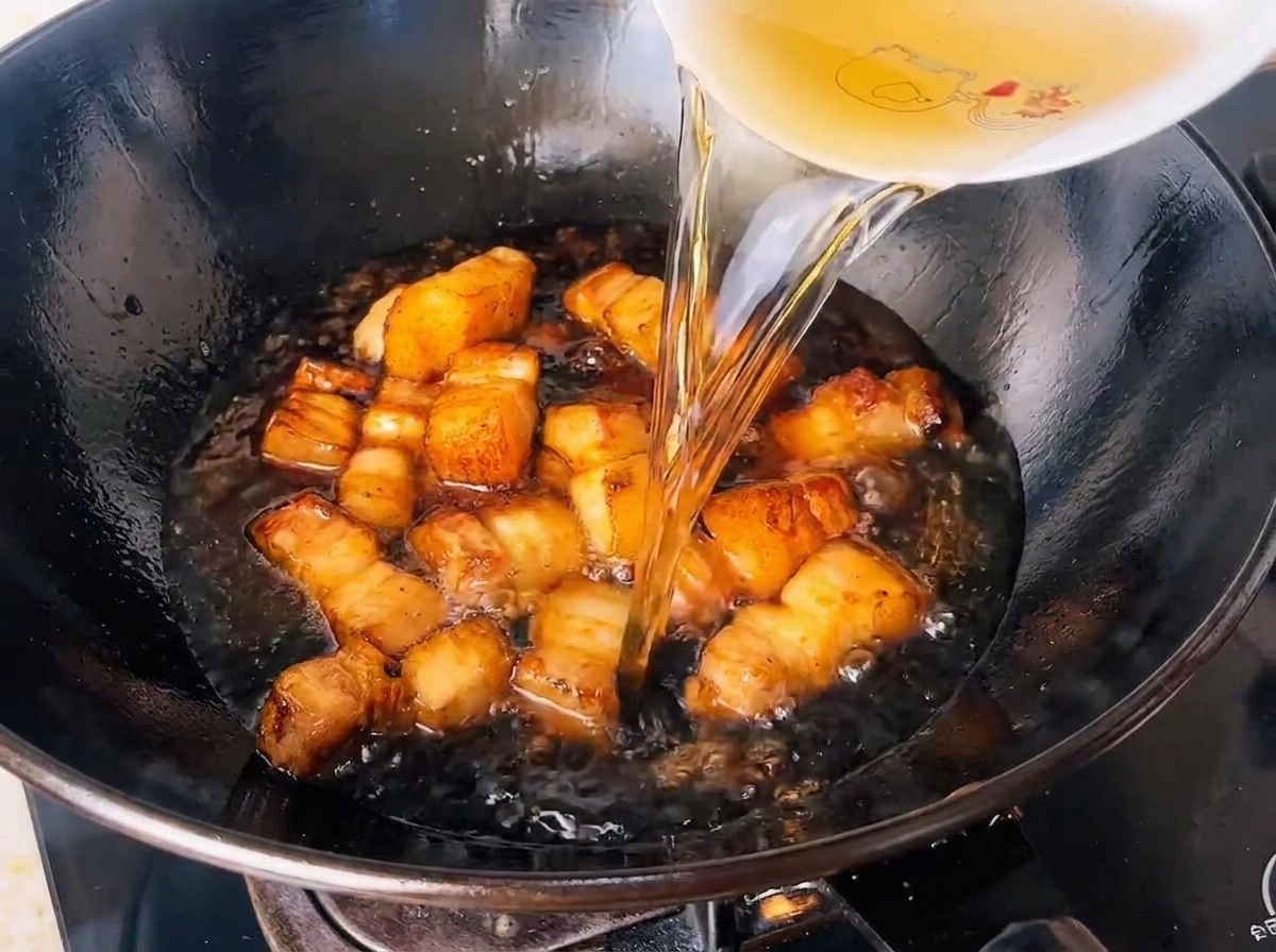 Agua de té verde infusionado vertiéndose en un wok lleno de cubos de panceta sazonados.