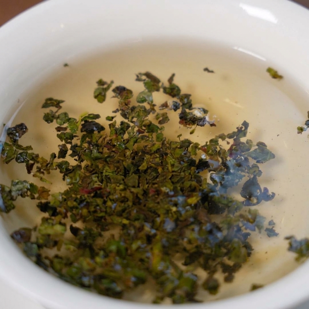 Hojas de té verde Tieguanyin expandiéndose en un cuenco blanco con agua caliente.