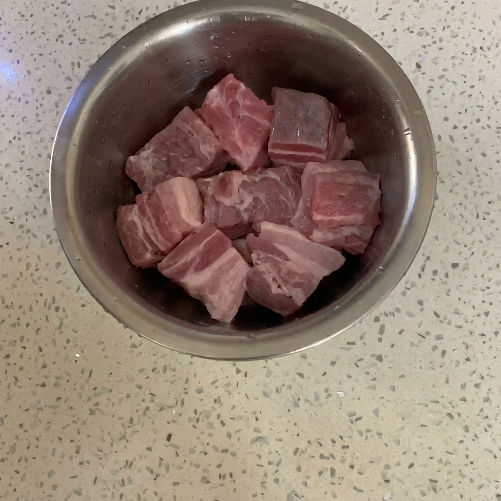 Cubos de panceta de cerdo cruda en un bol de acero inoxidable sobre una encimera.