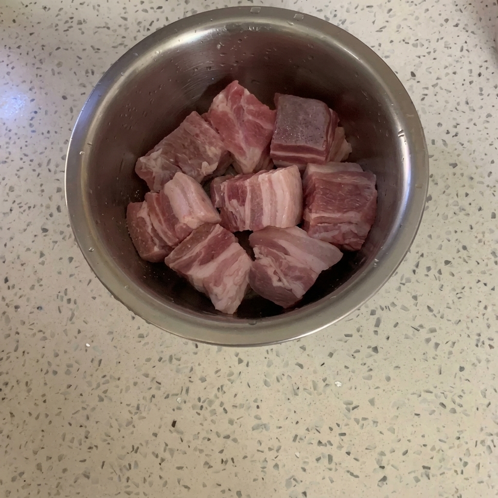 Bol de metal con panceta cruda siendo espolvoreada con pimienta molida.