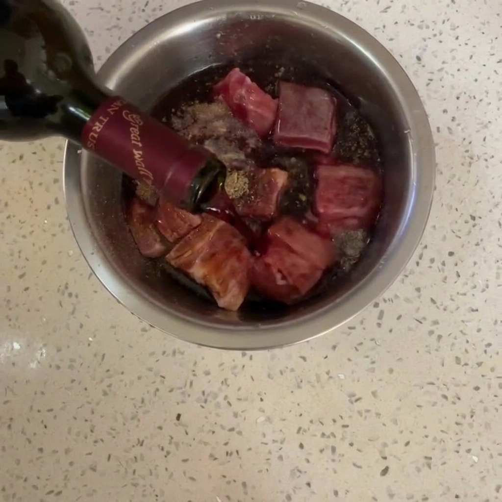 Vino tinto cayendo desde una botella sobre la carne sazonada.