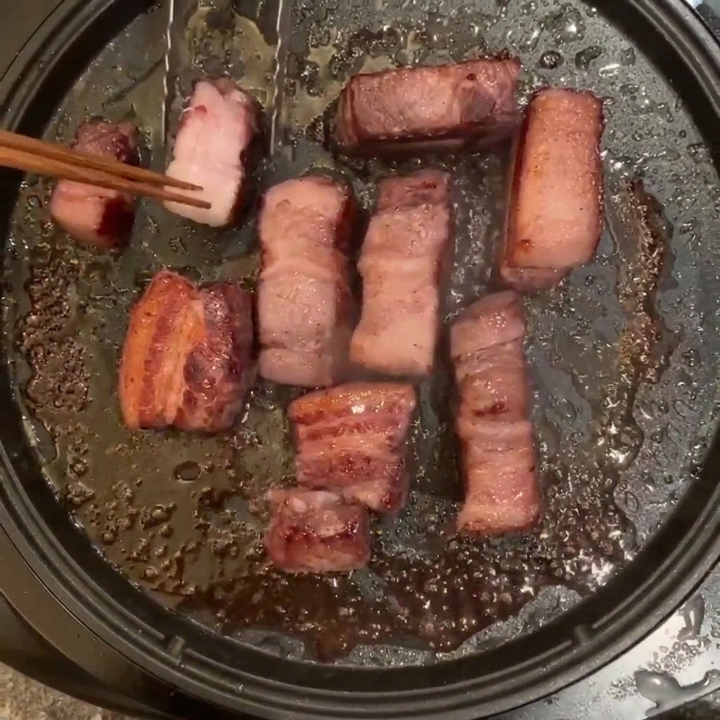 Trozos de panceta friéndose en una sartén y siendo removidos con palillos de madera.