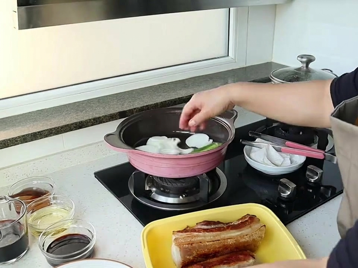 Una mano dejando caer trozos grandes de cebolla blanca en una sartén rosa para saltear.
