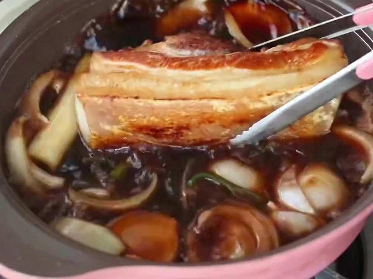 Pinzas colocando una tira gruesa de panceta sellada en una olla de líquido de braseado burbujeante con cebollas.