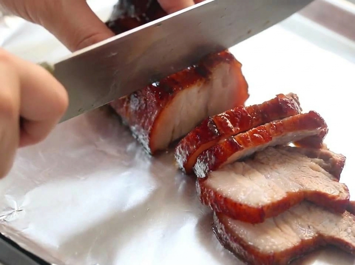 Un cuchillo de chef cortando a través de un trozo de panceta de cerdo al vino tinto glaseada descansando sobre papel de aluminio.
