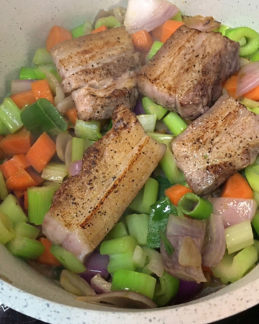 Trozos de panceta dorados sobre una base de verduras salteadas en una olla.