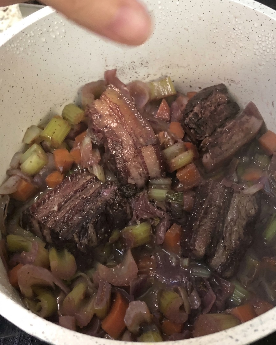 Pimienta negra recién molida sobre la olla de panceta estofada y verduras.