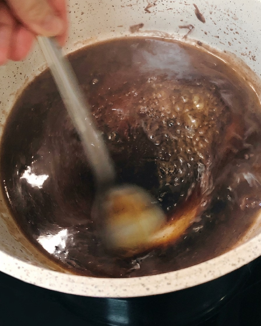 Reducción de vino tinto burbujeando y espesándose en la olla mientras se remueve.