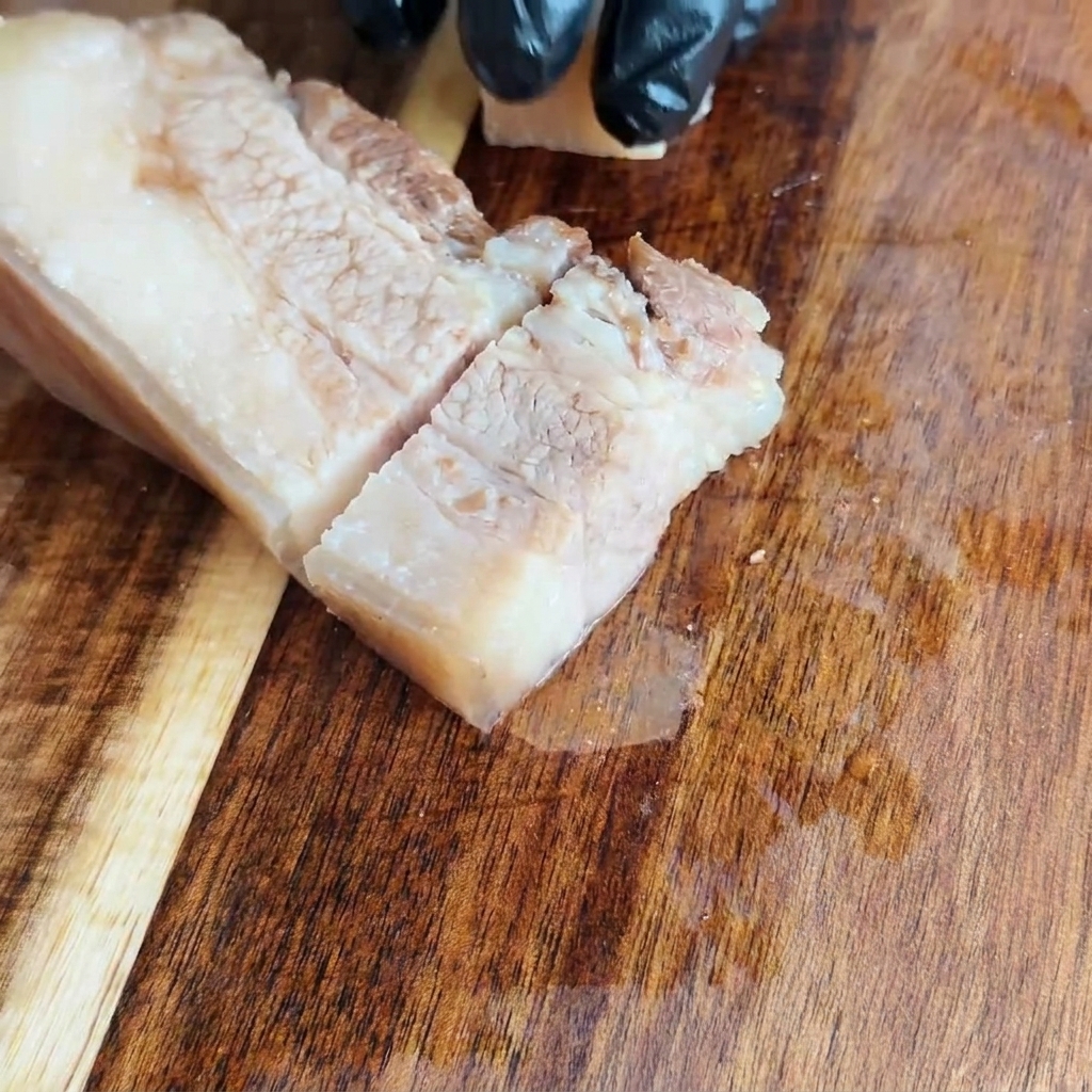 Panceta de cerdo fría siendo cortada en cuadrados uniformes sobre una tabla de cortar de madera.