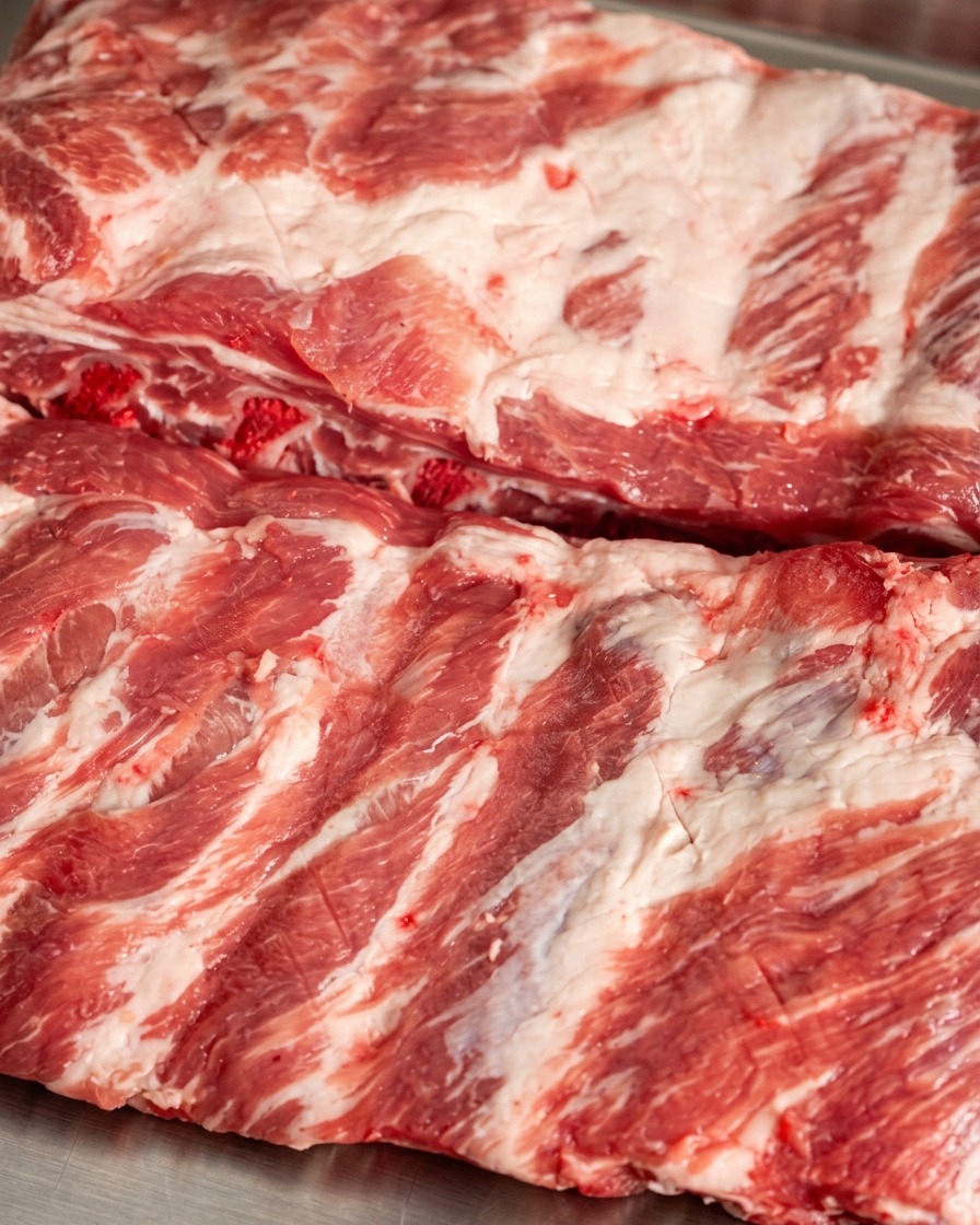Chile rojo en polvo y especias oscuras siendo espolvoreadas sobre la superficie de las costillas de cerdo marcadas.