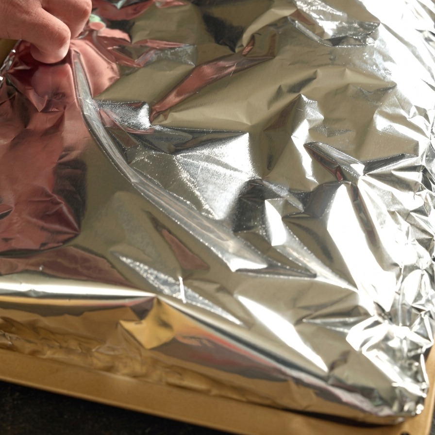 Manos doblando papel aluminio apretadamente sobre un costillar de cerdo sazonado.