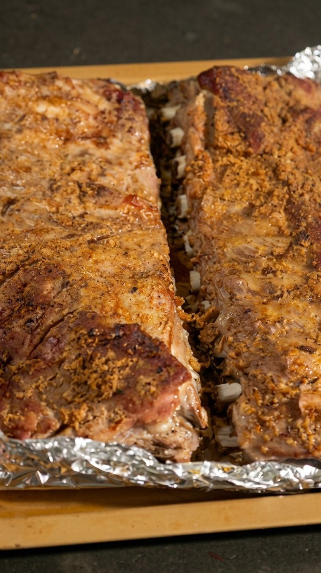 Dos costillares de cerdo cocidos en una bandeja con el papel aluminio abierto exponiendo la carne tierna.