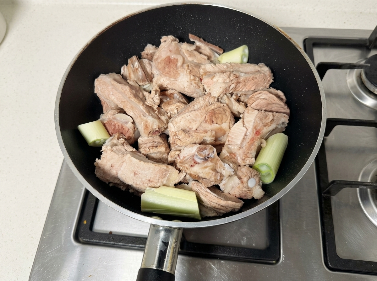 Costillas de cerdo crudas y trozos de cebollino en una sartén negra.