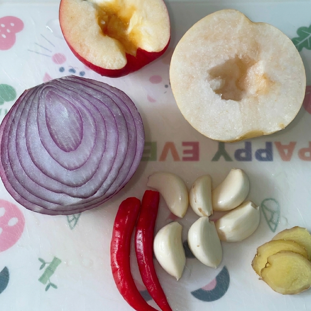 Manzana, cebolla roja, pera, dientes de ajo, chiles rojos y jengibre sobre una tabla de cortar.