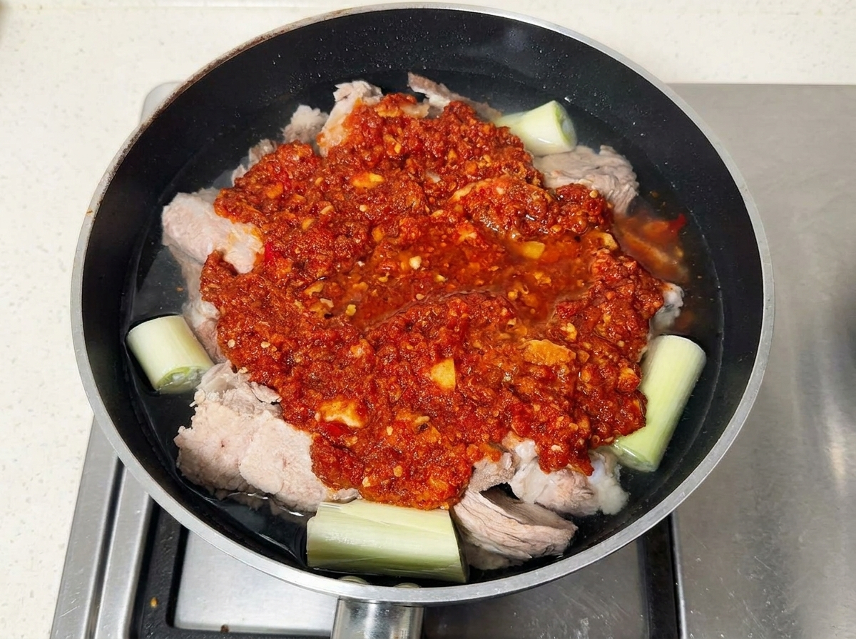 Costillas de cerdo cubiertas con pasta de chile rojo en una sartén llena de agua.