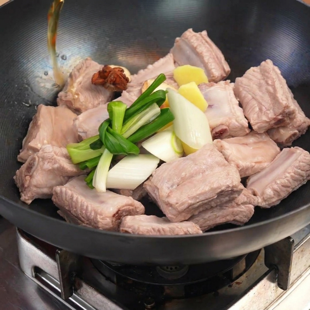 Costillas precocidas en un wok cubiertas con cebolletas anudadas, jengibre y anís estrellado mientras se vierte el líquido.