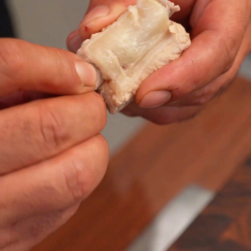 Manos retirando cuidadosamente el hueso de una pieza de costilla cocida y rellenándola con un pastel de arroz blanco cilíndrico.