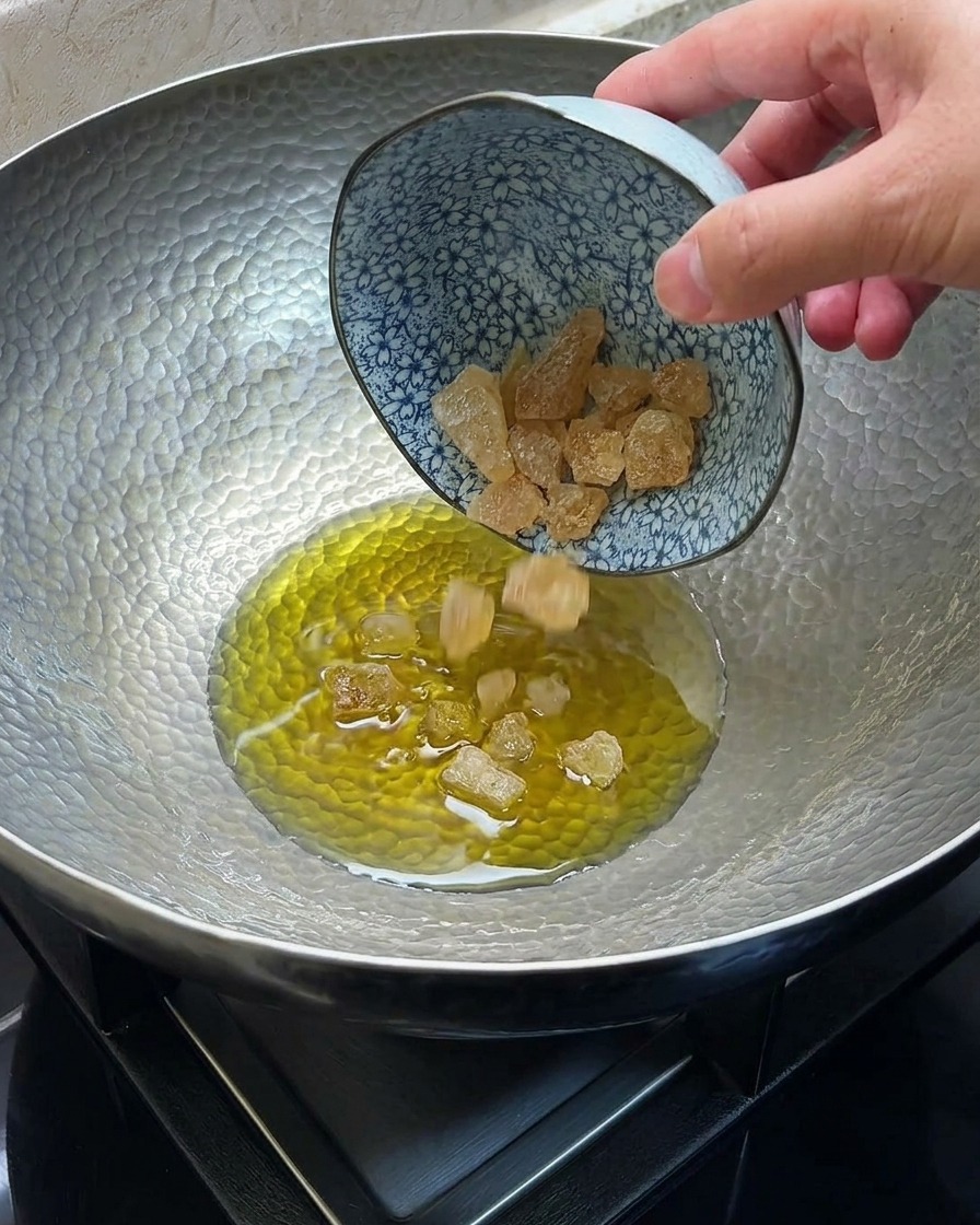 Azúcar roca derritiéndose y caramelizándose en aceite caliente dentro de un wok de metal.