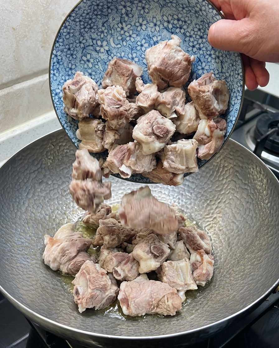 Costillas de cerdo salteándose en un wok con jengibre, anís estrellado y chiles secos.