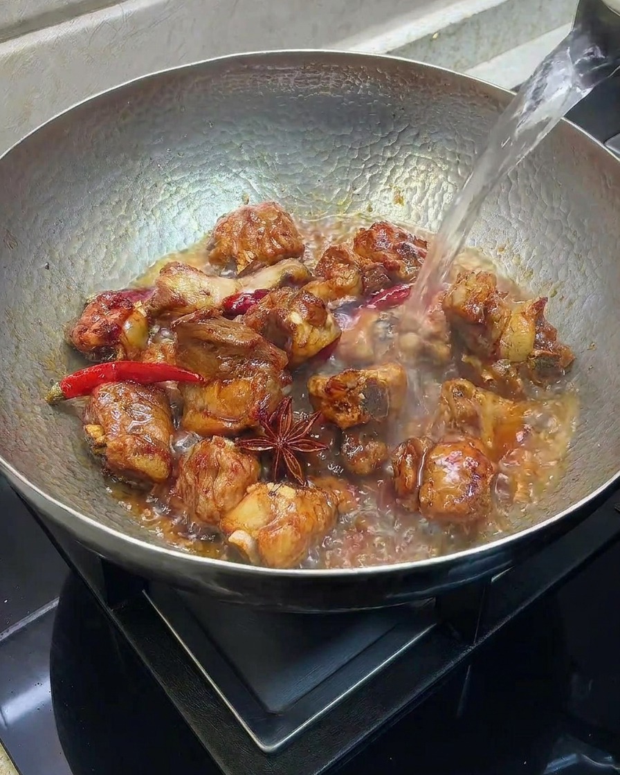 Agua caliente vertiéndose en un wok con costillas de cerdo selladas y especias.