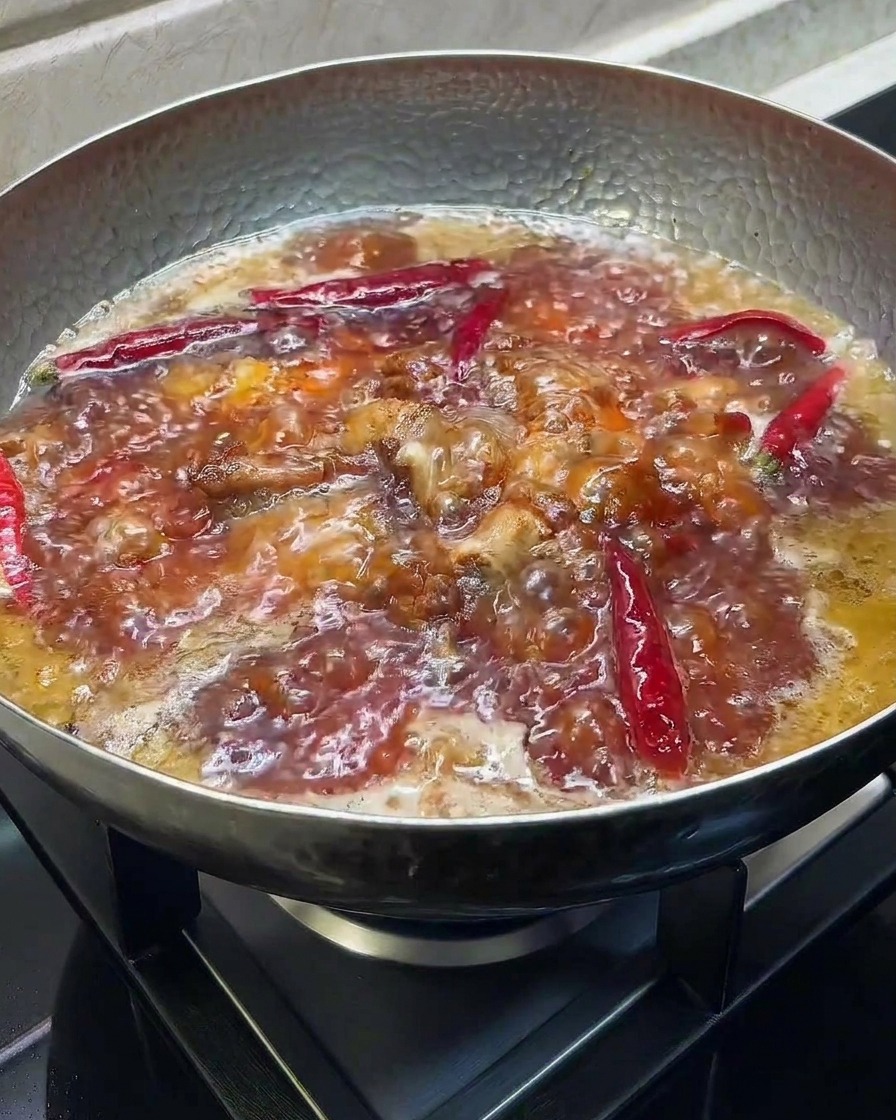 Salsa de soja oscura y vinagre siendo añadidos a una olla burbujeante con costillas estofadas.