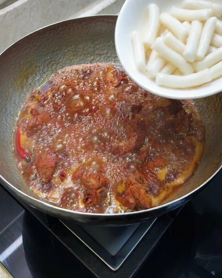 Pasteles de arroz cilíndricos blancos añadiéndose a una olla con costillas estofadas a fuego lento.