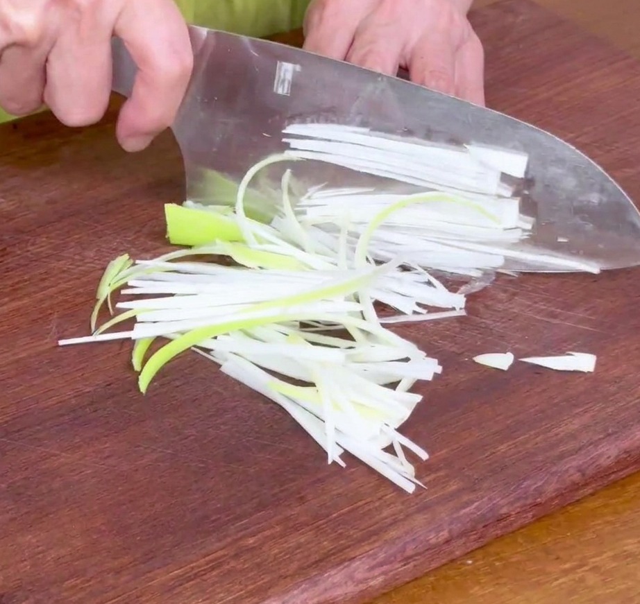 Tiras de cebolleta finamente cortadas sobre una tabla de madera, listas para la marinada.